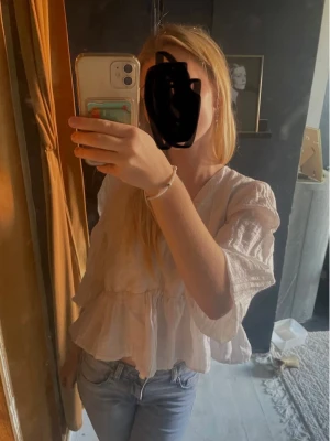Vit volangblus med v-ringning - Säljer en söt vit blus med v-ringning och volangdetaljer. Blusen har trekvartsärm och är tillverkad i ett lätt, luftigt tyg som ger en avslappnad och trendig look. Perfekt att matcha med jeans för en fräsch stil.