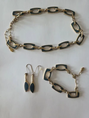 Set med halsband, armband och örhängen - Snyggt smyckeset med halsband, armband och örhängen i guld- och mörkblå metall. Halsbandet och armbandet har rektangulära länkar med blå emalj, och örhängena har droppformad design. Perfekt för dig som gillar unika accessoarer.