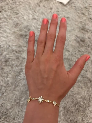 Guldigt armband med stjärnberlocker - Säljer ett snyggt armband i guldfärgad metall med flera stjärnformade berlocker dekorerade med glittrande stenar. Armbandet har en tunn kedja och gnistrar superfint i ljuset. Perfekt för dig som gillar detaljer som sticker ut och vill ha något unikt på handleden. Väldigt fint armband. Äkta guld