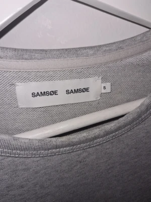 Ljusgrå sweatshirt från Samsøe Samsøe - En stilren ljusgrå sweatshirt från Samsøe Samsøe med rund halsringning och långa ärmar. Tröjan har en enkel och klassisk design, perfekt för en avslappnad look. Tillverkad i mjukt material för extra komfort.