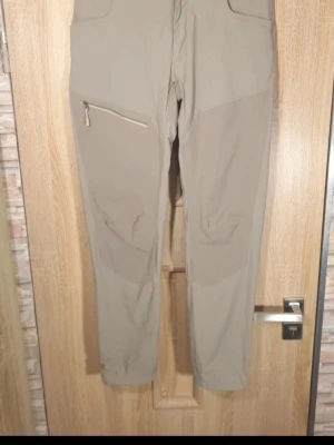 Beige cargobyxor från Haglöfs - Snygga beige cargobyxor från Haglöfs med dragkedjeförsedd ficka på benet och förstärkta partier vid knäna. Tillverkade i ett slitstarkt och stretchigt material som passar perfekt för aktiva dagar. Klassisk cargomodell med bälteshällor och flera fickor. Friluftsbyxa.