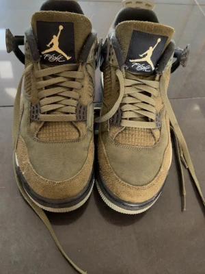 Olivgröna Air Jordan 4 sneakers (ÄKTA) - Säljer ett par olivgröna Air Jordan 4 sneakers med mockadetaljer och meshpaneler. Skorna har svarta och vita detaljer, klassisk Jumpman-logga på plösen och robust sula. Snygg high-top modell med coola plastdetaljer vid snörningen.