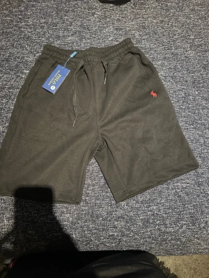 Svarta shorts från Polo Ralph Lauren - Svarta shorts från Polo Ralph Lauren med klassisk röd broderad logga på benet. Shortsen har elastisk midja med snörning och är tillverkade i mjuk bomull, perfekta för en avslappnad stil.