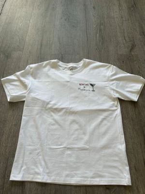 Saint Barth inpsired t-shirt med broderi Bikini & Martini - Saint Barth inspired Vit t-shirt med broderad text 'Bikini & Martini' och en martiniglas-illustration på bröstet. Klassisk passform med rund hals och korta ärmar. Perfekt för en chill och avslappnad stil.