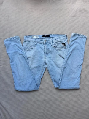 Replay Anbass - Säljer ett par ljusblå skinny jeans från Replay med klassisk femficksmodell och snygga detaljer som Replay-logga på fickan och läderpatch bak i midjan. Jeansen har normalhög midja och är tillverkade i mjuk denim med stretch för extra komfort. W30 L32
