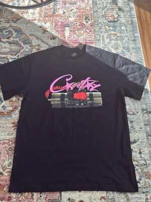 Cortiez T-shirt - Cool svart t-shirt med färgglatt tryck framtill och stor text 'NO TIME 4 LUV' på ryggen. T-shirten har korta ärmar och en relaxed passform. Perfekt för dig som gillar streetwear och statement-plagg.