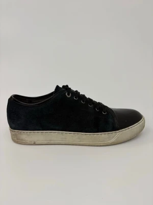 Svarta sneakers med lackdetalj - Stilrena svarta sneakers med ovandel i mocka och glansig lackad tå. Skorna har vita sulor och svarta skosnören. Perfekta för dig som gillar en clean look med lite edge.