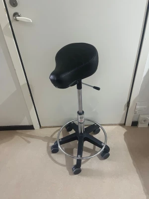 Sadelstol med PUCH-sadel - Unik sadelstol med svart PUCH-sadel som sits, monterad på en höj- och sänkbar metallstomme med fem hjul och fotring. Sitsen är klädd i svart konstläder och har PUCH-logga i vitt på baksidan. Perfekt för dig som jobbar på ex kontor. 