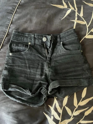 Svarta high waist jeansshorts - Snygga svarta high waist jeansshorts med råa kanter och femficksmodell. Klassisk knapp och dragkedja framtill samt bälteshällor. Perfekta till sommaren för en avslappnad och trendig look. Använt kanska mycke men fungerar endå