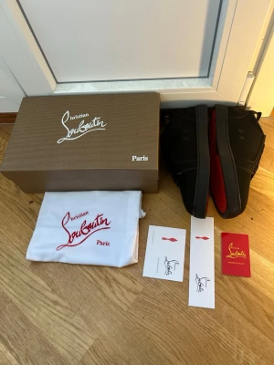 Svarta Christian Louboutin sneakers - Säljer ett par svarta Christian Louboutin sneakers med den ikoniska röda sulan. Skorna har en klassisk high-top design och är tillverkade i svart mocka med svarta snören. Kommer med originalkartong, dustbag och äkthetskort.