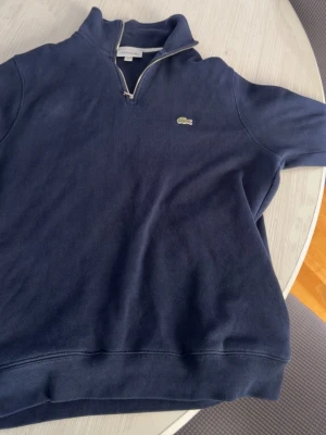 Lacoste half-zip - Stilten mörklblå halvzip från lacoste. Passar till varje säsong och är i utmärkt skick. Ljuset är lite dåligt i bilderna men denna tröjan är i nyskick.  Storlek L men sitter mer som M