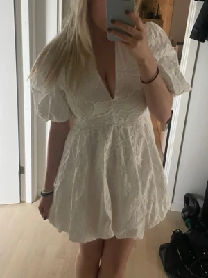 Vit kort klänning med puffärm - Supersöt vit kort klänning med puffärmar och  v-ringning. Klänningen har ett broderat blommönster. Använd endast en gång på studenten! (De två sista bilderna är lånade men samma klänning) 