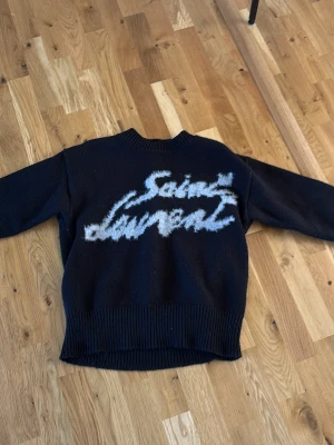Svart stickad YSL tröja - Säljer min YSL tröja för att jag helt enkelt inte har mer plats för den i garderoben, däremot är den otroligt skön och sitter perfekt för både S och M.