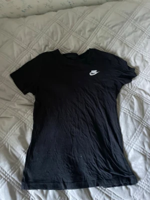 Svart Nike T-shirt XS - Snygg svart T-shirt från Nike i storlek XS. Klassisk modell med korta ärmar och rund hals. Liten vit Nike-logga på bröstet. Tillverkad i mjuk bomull som är skön att ha på sig. Perfekt till jeans eller shorts för en sportig vibe.