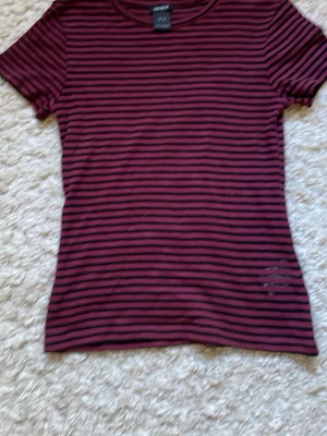 Vinröd och svart randig t-shirt Lindex - Säljer denna söta coola toppen från Lindex. Aldrig använt denna så den är i princip som ny. 
