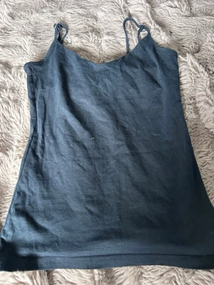 Mörkblå linnetopp med smala axelband - En enkel och stilren mörkblå linnetopp med smala axelband. Toppen har en rak passform och är perfekt för varma dagar eller som layering-piece. Materialet känns mjukt och bekvämt mot huden.