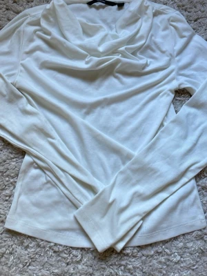 Vit långärmad topp från Vero Moda - Snygg vit långärmad topp från Vero Moda med draperad halsringning. Tillverkad i mjukt material som känns skönt mot huden. Perfekt att styla med jeans eller kjol för en clean och fräsch look.