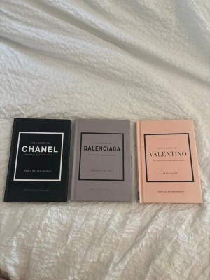 Lilla boken om Chanel, Balenciaga & Valentino - Säljer tre snygga coffee table-böcker: Lilla boken om Chanel (svart), Balenciaga (grå) och Valentino (ljusrosa). Böckerna har hårda omslag och stilren design, perfekta för modeintresserade och som inredningsdetalj.