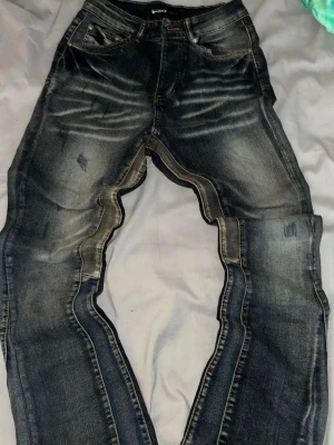 Purple jeans märket Mörkblå slitna jeans med tvättade detaljer - Säljer ett par mörkblå jeans med snygga slitningar och tvättade detaljer. Jeansen har fem fickor, normal midja och raka ben. Materialet är klassisk denim och de har en cool, avslappnad look som passar perfekt till streetwear.