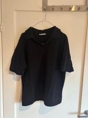 Svart kortärmad skjorta Zara - En svart kortärmad skjorta från Zara med klassisk krage och relaxed fit. Skjortan är tillverkad i mjuk bomull och har en enkel, stilren design utan synliga knappar framtill. Perfekt för en clean och avslappnad look.