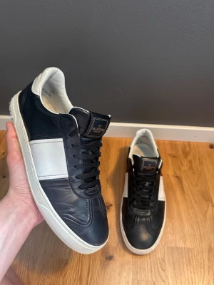 Svarta och vita sneakers från Valentino - Snygga sneakers från Valentino i svart och vitt läder. Klassisk låg modell med svart ovandel, vit sidopanel och vita detaljer. Skorna har svarta skosnören och en vit yttersula. Perfekta för dig som gillar stilrena och exklusiva sneakers.