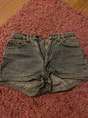 Högmidjade jeansshorts från Levi's - Snygga högmidjade jeansshorts från Levi's i klassisk blå denim. Modellen har fem fickor, bälteshällor och dragkedja framtill. Passformen är loose och shortsen har en tidlös look med slitna detaljer och Levi's ikoniska bakfickor. Vet inte riktigt storleken men skulle gissa på 40💗💗