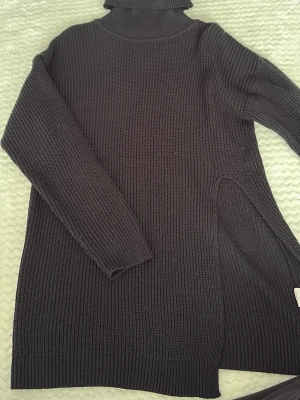Svart polotröja med slitsar - Stickad svart polotröja med långa ärmar och höga slitsar i sidorna. Tröjan har en ribbstickad struktur och en hög polokrage som ger en cool och avslappnad look. Perfekt att styla med jeans eller leggings.