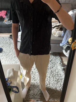 Svart kortärmad skjorta från 157 - Svart skjorta från 157 i storlek M. Skjortan har korta ärmar, klassisk krage och knäppning framtill. Enkel och stilren design som passar perfekt till jeans eller chinos.