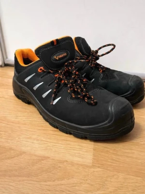 Svarta kängor från Gesto med orange detaljer - Säljer ett par svarta kängor från Gesto, modell Balder. De har orange foder och snören med svarta och orange detaljer. Ovandelen är i slitstarkt material med reflexdetaljer på sidorna. Perfekta för dig som vill ha både stil och funktion.