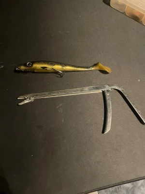 Guldfärgad jigg och kroklossare - Säljer ett fiskeset med en guldfärgad jigg i mjukplast med svart mönster och stor ögla samt en metallisk kroklossare. Perfekt för dig som gillar fiske och vill ha bra utrustning till gädda eller abborre.