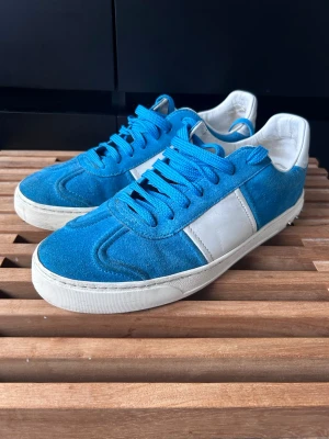 Valentino flycrews  - Snygga blåa sneakers från Valentino med vit sula och vita detaljery på sidan. Ovandelen är i mocka och skorna har matchande blå skosnören. Klassisk låg modell som passar perfekt till jeans eller shorts.