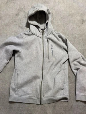 Sail Racing Hoodie Zip-Up Grå – Strl M - Säljer en grå Sail Racing hoodie med dragkedja och huva. Stilren och bekväm modell med fickor och bröstficka med dragkedja. Perfekt för vardag och fritid.  📏 Storlek: M ✅ Original Sail Racing ✅ Fint skick ✅ Dragkedja framtill ✅ Huva och flera fickor