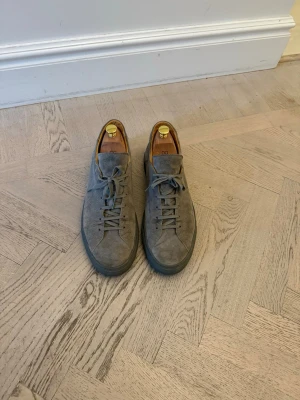 Grå sneakers i mocka från CQP - Stilrena grå sneakers från CQP i mjuk mocka med matchande grå snörning och sula. Lågt skaft och minimalistisk design gör dem lätta att matcha med olika outfits. Skorna har en lyxig känsla tack vare materialvalet och detaljerna invändigt. Nypris 3800kr.