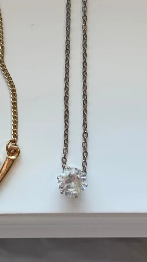 Silverhalsband med stor klar sten - Snyggt halsband i silverfärgad metall med en stor, rund klar sten som hänge. Kedjan är tunn och stilren vilket gör att den gnistrande stenen verkligen står i fokus. Perfekt för dig som gillar minimalistiska smycken med lite extra bling.