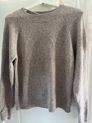 Beige stickad tröja från Vero Moda - Mysig beige stickad tröja från Vero Moda med rund halsringning och ribbade muddar vid ärmslut och nederkant. Tröjan har en enkel och stilren design som passar perfekt till jeans eller kjol. Materialet känns mjukt och bekvämt mot huden.