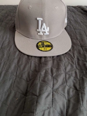 La keps grå - Säljer en grå fitted keps från New Era, modell 59FIFTY, med LA Dodgers-logga broderad i vitt framtill. Klassisk rak skärm och MLB-logga baktill. Tillverkad i bomullstyg och riktigt clean look.