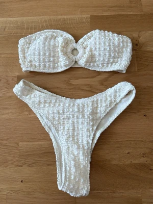 Vit bandeau bikini med struktur - Säljer en snygg vit bandeau bikini med strukturerat tyg och en rund detalj i mitten av toppen. Oanvänd💞