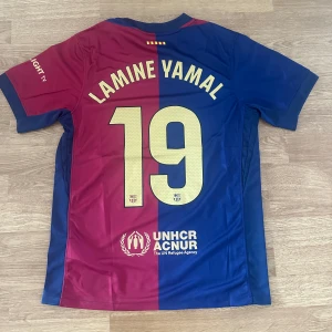 FC Barcelona X Travis Scott Lamine Yamal #19 - Exklusiv Fc Barcelona hemma tröja i samarbete med Travis Scott. Det här är en unik tröja då laget bar den under El clasicon mot Real Madrid. Lamine Yamal 19 på ryggen. Helt ny!