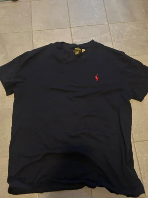 Mörkblå t-shirt från Polo Ralph Lauren - Klassisk mörkblå t-shirt från Polo Ralph Lauren med röd broderad logga på bröstet. T-shirten har rund halsringning och korta ärmar. Perfekt basic-plagg med snygg passform och mjukt bomullsmaterial.