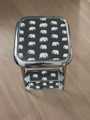 Beslag/klädsel till Awab/Lindkvist kökspall/stegpall Svenskt Tenn motiv Estrid - Beslag/klädsel till Awab/Lindkvist  Färdigklippt klädsel till stegpall. Motiv Svenskt Tenn Elefant Grå. Avtorkningsbar laminerad yta.  Klippbara med sax som sedan limmas fast med kontaktlim eller dubbelhäftande tejp på stegpallen.  Obs! Pallen på bilden ingår ej utan används endast för att visa hur beslagen ska användas.  Vid köp ange i samband med betalning om du har en AWAB eller Lindkvist pall