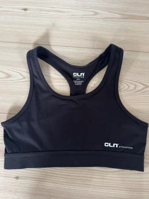Svart sport-bh från CLN Athletics - Svart sport-bh från CLN Athletics med brottarrygg och elastisk resår nedtill. Tillverkad i ett stretchigt och fukttransporterande material som passar perfekt för träning. Diskret logga framtill i vitt.