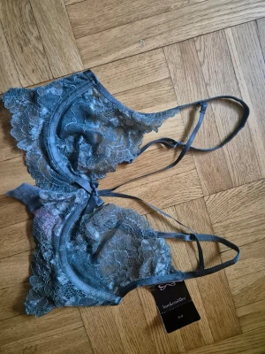 Grön spets-bh från Hunkemöller 70C NY! - Säljer en snygg grön bh från Hunkemöller i genomskinlig spets med blommigt mönster. Bh:n har justerbara axelband, dekorativ rosett framtill och hakknäppning bak. Perfekt för dig som gillar en feminin och trendig stil. Ny med lappar kvar!