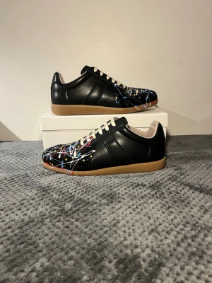 Maison Margiela Skor - Säljer ett par svarta Maison margiela skor med paintsplatter. Skick 9/10. Storlek 43. Skriv om ni undrar något!