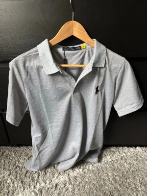 Grå pikétröja från Polo Ralph Lauren passar S - Klassisk grå pikétröja från Polo Ralph Lauren med korta ärmar och krage. Tröjan är storlek M men passar storlek S! Tröjan är nytt skick och inga skador, pris kan diskuteras. Hör av er vid funderingar!