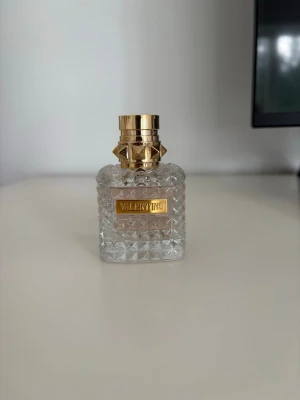 Valentino Donna Eau de Parfum 30ml - Elegant parfym från Valentino i en lyxig, transparent glasflaska med nitar och gulddetaljer. Flaskan har en fyrkantig form och ett guldigt lock. Medföljer gör en rosa och guldig förpackning. Perfekt för dig som gillar exklusiva dofter. (Kan gå med på lägre pris) NÄSTAN ALDRIG ANVÄND! Nypris är 1000🤍🤍