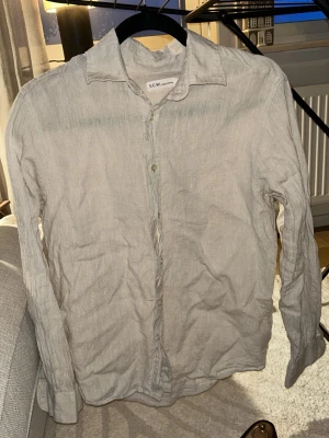 Beige linneskjorta från S.C.W. - Säljer pojkvännens linneskjorta pga att den har blivit för liten tyvärr🤎Använd fåtal gånger! Luftig och stilren beige skjorta från S.C.W. i 100% linne. Skjortan har klassisk krage, långa ärmar och knappar framtill. Perfekt för varma dagar och enkel att styla till olika outfits. 
