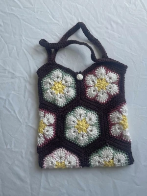 Handgjord virkad liten shoppingväska - Unik liten shoppingväska som är handvirkad med blommönster i vitt, gult, grönt och vinrött. Väskan har sexkantiga paneler och ett dekorativt vitt knappstängning. Korta handtag. Perfekt för dig som gillar retro och färgglada accessoarer. Materialet är bomulls garn.
