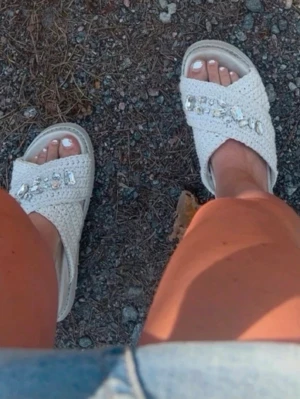 Sommartofflor - Säljer ett par vita sandaler med breda, korslagda flätade band och stora strassdetaljer på ovansidan. Sandalerna har en chunky sula i vitt och öppen tå. Perfekta för dig som vill ha en trendig och bekväm look i sommar.