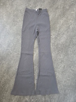 Grå ribbade utsvängda leggings Stl XS  - Säljer ett par grå leggings med ribbad struktur och utsvängda ben. Perfekta för dig som gillar en trendig och bekväm stil. Midjehög passform och stretchigt material som sitter snyggt på kroppen. Innerbenslöngd ca 73 cm , materialet är 58 % bomull 38 % polyester och 4 % elastan 