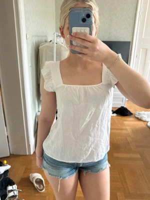 Vit blus med volangärmar - Söt vit blus med fyrkantig ringning och volangdetaljer vid armbanden. Aldrig använd men prislappen borttagen☺️💞